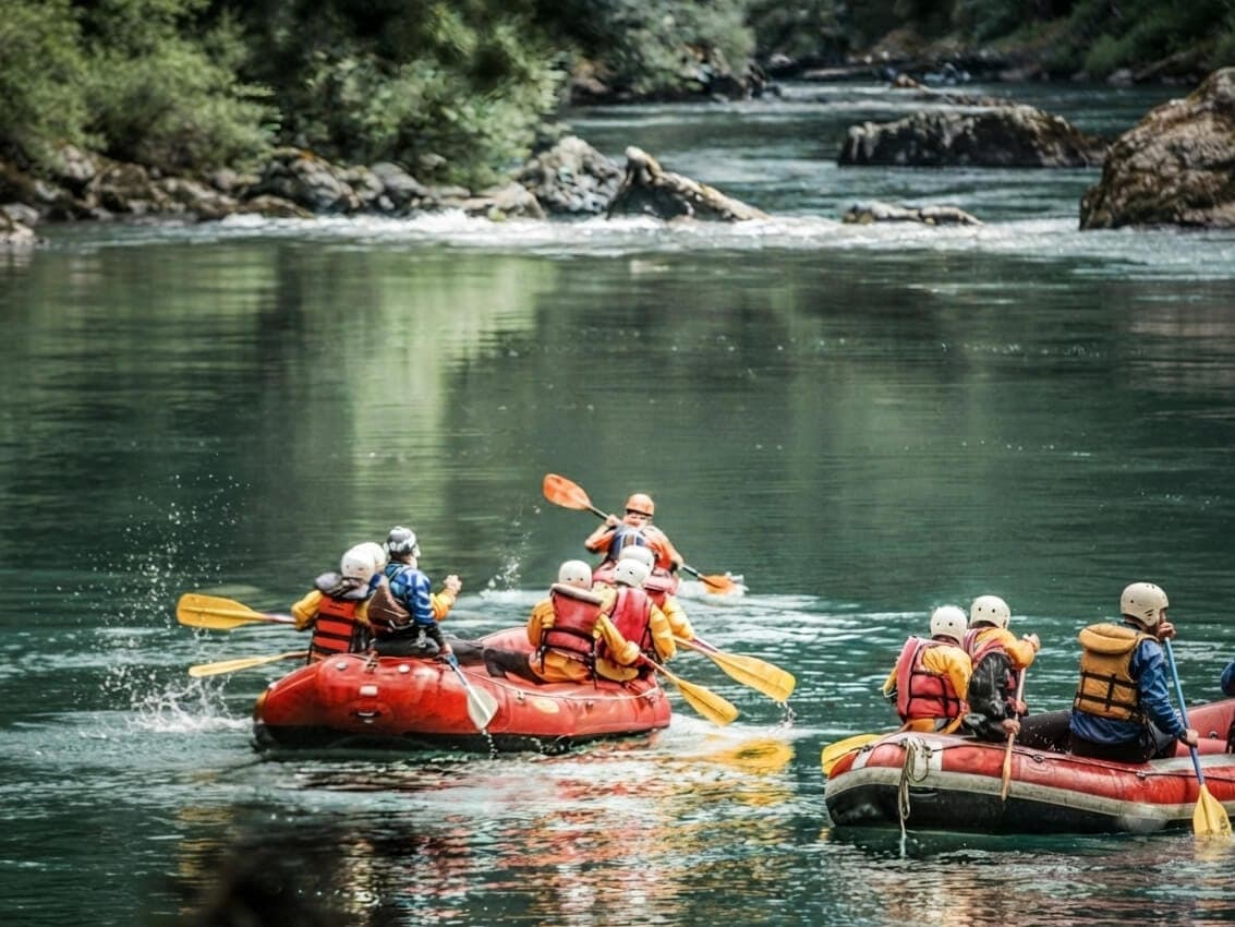 Dos botes de rafting bajando sin apuro un tramo ancho y calmo del río Manso, con el bosque reflejado en el agua.